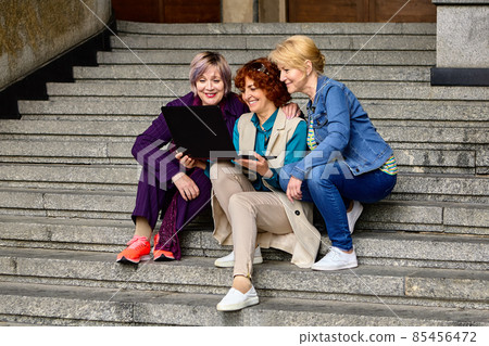 Live streaming classes using laptop by three middle aged women outdoors. 85456472