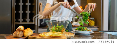 salad concept the female in white top and white and blue plaid turban using a spatula to get the salad from the mixing bowl on the plate salad concept the female in white top and white and blue plaid turban using a spatula to get the salad from the mixing bowl on the plate 85456914