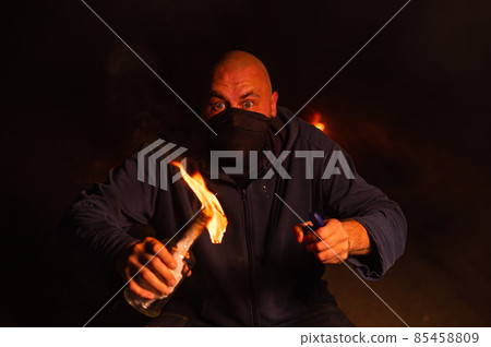 A masked man is holding a burning bottle. Molotov cocktail. A masked man is holding a burning bottle. Molotov cocktail. 85458809