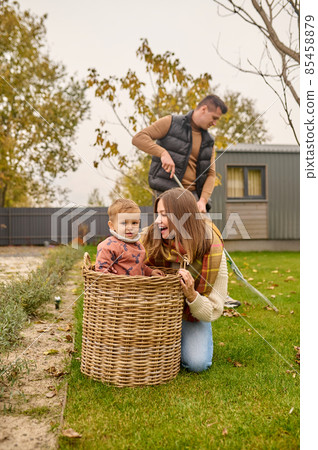 Joyful woman crouching looking at child in basket outdoors 85458879
