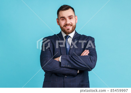Young happy successful businessman wearing official style suit posing with happy confident expression, looking at camera, keeping arms folded. Indoor studio shot isolated on blue background. Young happy successful businessman wearing official style suit posing with happy confident expression, looking at camera, keeping arms folded. Indoor studio shot isolated on blue background. 85459997