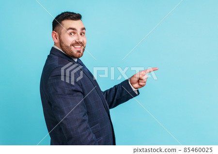 Wow, look at ads here. Side view of bearded businessman wearing official style suit pointing aside, showing blank copy space for idea presentation. Indoor studio shot isolated on blue background. 85460025