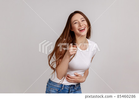Hey, you are ridiculous. Joyful woman laughing, holding stomach, pointing to camera, taunting you, can't stop hysterical laughter, wearing white T-shirt. Indoor studio shot isolated on gray background 85460286