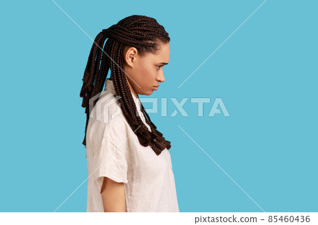Side view of offended woman with dreadlocks looking with sulking frowning face, waits for explanations or apology, being irritated with unfair thing. Indoor studio shot isolated on blue background. Side view of offended woman with dreadlocks looking with sulking frowning face, waits for explanations or apology, being irritated with unfair thing. Indoor studio shot isolated on blue background. 85460436