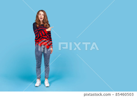 Wow, look, advertise here. Full length portrait of woman showing copy space with shocked expression, showing blank wall for crazy commercial idea. Indoor studio shot isolated on blue background. Wow, look, advertise here. Full length portrait of woman showing copy space with shocked expression, showing blank wall for crazy commercial idea. Indoor studio shot isolated on blue background. 85460503