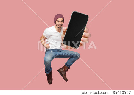 Happy man flying and jumping in air and showing big mobile empty screen for copy space and advertising area. indoor studio shot isolated on pink background 85460507