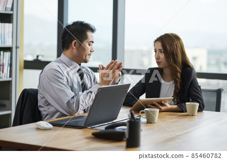 asian businessman and businesswoman sitting at desk in office discussing business asian businessman and businesswoman sitting at desk in office discussing business 85460782