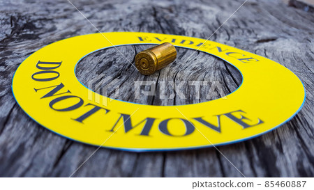 Bullet shell in middle of a yellow circle with text "evidence do not move" the circle on black background, concept for crime scene investigation 85460887