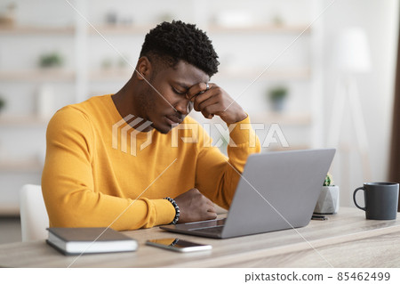 Tired african american manager working on laptop, touching head Tired african american manager working on laptop, touching head 85462499