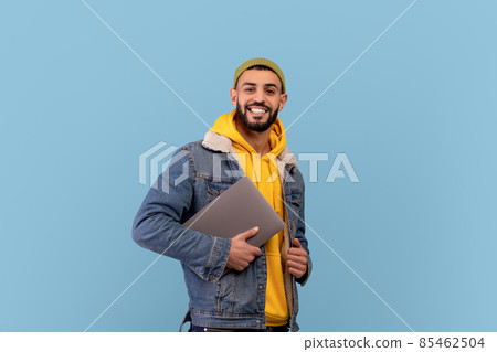 Happy middle eastern guy holding laptop and smiling at camera, arabic man with pc computer over blue background Happy middle eastern guy holding laptop and smiling at camera, arabic man with pc computer over blue background 85462504