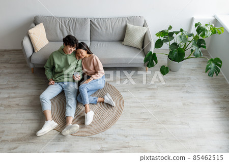 Cheery Asian couple using smartphone application, relaxing on sofa at home on weekend, top view. Copy space 85462515
