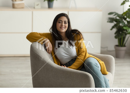 Happy arab lady sitting in comfy armchair and smiling at camera, enjoying lazy morning, having peaceful weekend at home Happy arab lady sitting in comfy armchair and smiling at camera, enjoying lazy morning, having peaceful weekend at home 85462630