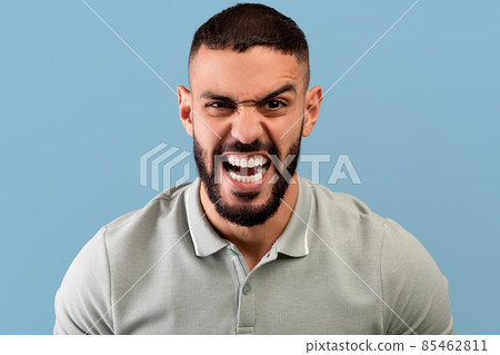 Portrait of furious arab man shouting with rage at camera, screaming with fury, standing over blue background 85462811