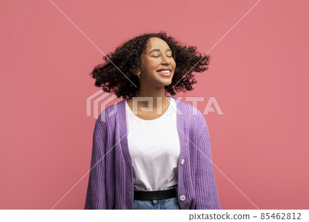 Portrait of smiling African American female model posing with healthy curly flying hair on pink studio background Portrait of smiling African American female model posing with healthy curly flying hair on pink studio background 85462812