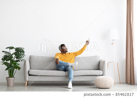 Relaxed african american guy sitting on couch, turning on AC Relaxed african american guy sitting on couch, turning on AC 85462817