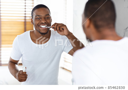 Happy Young African American Man Brushing His Teeth With Toothbrush In Bathroom Happy Young African American Man Brushing His Teeth With Toothbrush In Bathroom 85462830