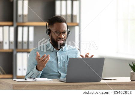 Disgruntled shocked sad young african american bearded male in glasses, headphones gestures and works on pc Disgruntled shocked sad young african american bearded male in glasses, headphones gestures and works on pc 85462998