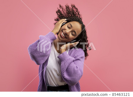Carefree African American lady listening to music in wireless headphones, dancing with closed eyes on pink background 85463121