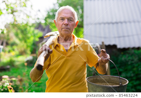 Senior man standing in yard of his country house with gardening tools 85463224