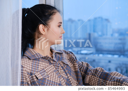 Young woman in warm shirt and socks sitting on windowsill and looking to the window 85464993