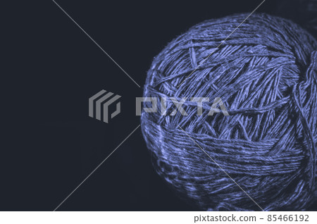 A ball of yarn on a black background. Material for knitting. Home crafts and hobbies. Colored in trendy color of year 2022 Very Peri. Selective focus, copy space. 85466192