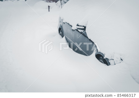 A car abandoned on the road is covered with snow. The consequences of the past snowstorm. Winter cataclysm, an abnormal amount of snow falling. Selective focus A car abandoned on the road is covered with snow. The consequences of the past snowstorm. Winter cataclysm, an abnormal amount of snow falling. Selective focus 85466317