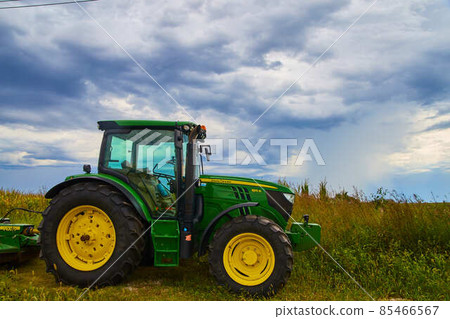 Farming tractor equipment John Deer with stormy clouds Farming tractor equipment John Deer with stormy clouds 85466567