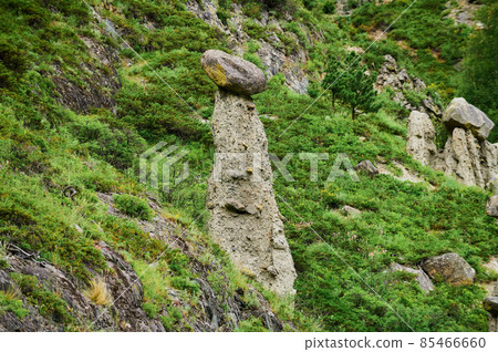 High rock formation with stone boulders at the top, standing on the side of a hill. Stone mushrooms, Altai, Siberia, Russia. 85466660