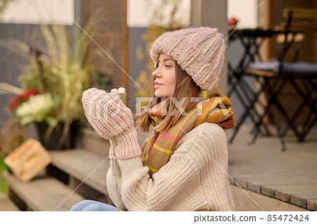 Woman with cup sideways to camera sitting on veranda 85472424