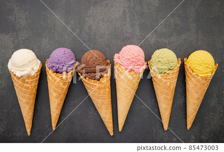 Various of ice cream flavor in cones blueberry ,pistachio ,almond ,orange and chocolate setup on dark stone background . Summer and Sweet menu concept. 85473003