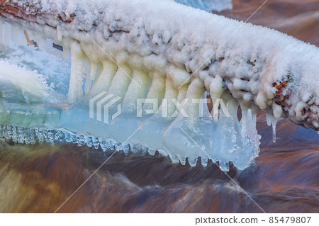 Icicles over the water in the river. Natural landscape. Winter. Background image. Icicles over the water in the river. Natural landscape. Winter. Background image. 85479807