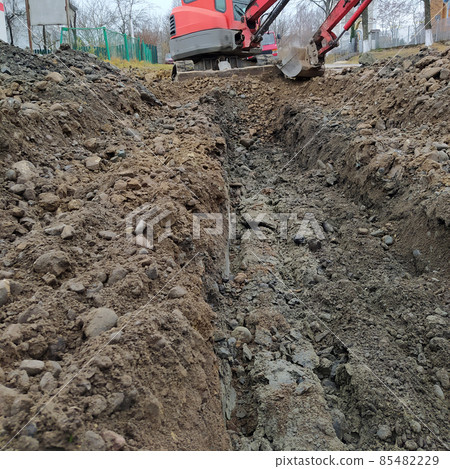 An excavator digs a trench for sewage and rainwater along the side of the road. An excavator digs a trench for sewage and rainwater along the side of the road. 85482229