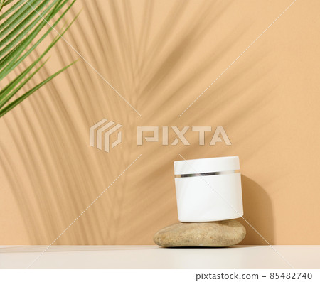 white round plastic jar for cosmetic products on a brown background. Palm leaf shadow. Blank for branding products, mock up white round plastic jar for cosmetic products on a brown background. Palm leaf shadow. Blank for branding products, mock up 85482740