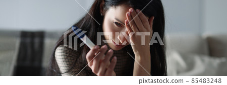 Upset woman holding pregnancy test while sitting on couch Upset woman holding pregnancy test while sitting on couch 85483248