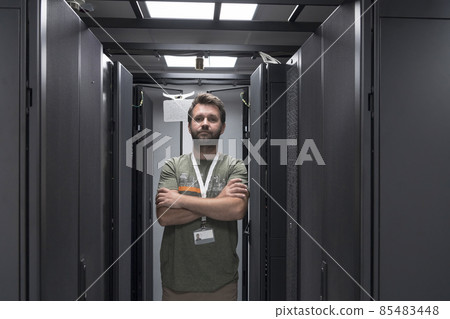 Portrait of male technician or network administrator standing brave as a hero with arms crossed in data center server room. 85483448