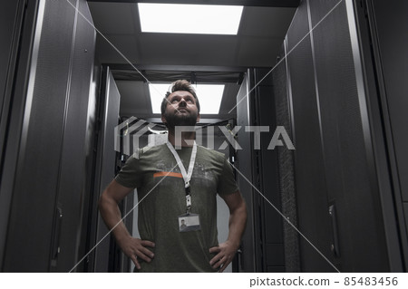 Portrait of male technician or network administrator standing brave as a hero with arms crossed in data center server room. Portrait of male technician or network administrator standing brave as a hero with arms crossed in data center server room. 85483456