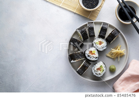 Sushi on round plate with chopsticks, soy sauce. ginger. Homemade rolls with salmon, avocado and cucumber. 85485476