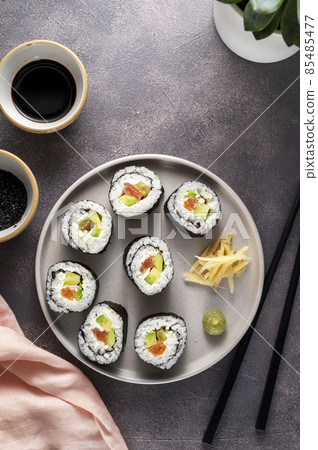Sushi on round plate with chopsticks, soy sauce. ginger. Homemade rolls with salmon, avocado and cucumber. 85485477