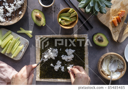 Cooking Sushi rolls at home with salmon, avocado and cucumber. Female hand preparing avocado sushi, step by step. 85485485