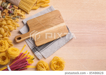 Different types of pasta and cutting board on wooden table, flat lay 85486628