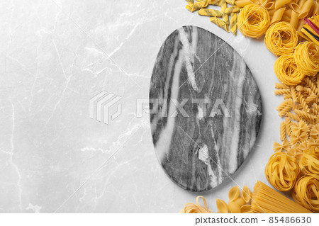Different types of pasta and empty board on light grey marble table, flat lay. Space for text Different types of pasta and empty board on light grey marble table, flat lay. Space for text 85486630