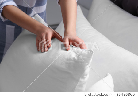 Woman fluffing white pillow on bed, closeup Woman fluffing white pillow on bed, closeup 85486869
