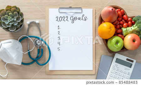 2022 New Year Goals in new normal lifestyle, work-life balance with face mask safety awareness from covid-19, healthy food, good heart health, blank resolution list on white paper medical clipboard 85488483