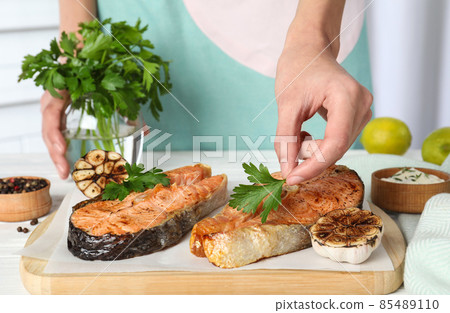 Woman adding parsley to cooked red fish on white wooden table, closeup 85489110