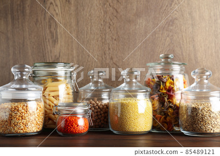 Glass jars with different types of groats and pasta on wooden table Glass jars with different types of groats and pasta on wooden table 85489121