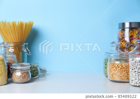 Glass jars with different types of groats and pasta on white wooden table 85489122