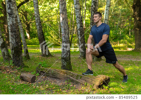 A young enduring athletic athlete is doing stretching in the forest outdoors, around the forest, trees. Active forest, workout outdoor training marathon, trees wellbeing. Adult body running A young enduring athletic athlete is doing stretching in the forest outdoors, around the forest, trees. Active forest, workout outdoor training marathon, trees wellbeing. Adult body running 85489525
