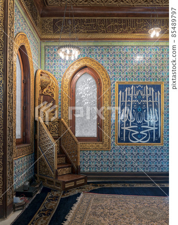 Wooden golden ornate minbar (Platform), wooden arched window framed by golden ornate floral pattern, and ceramic tiles wall with floral blue patterns Wooden golden ornate minbar (Platform), wooden arched window framed by golden ornate floral pattern, and ceramic tiles wall with floral blue patterns 85489797