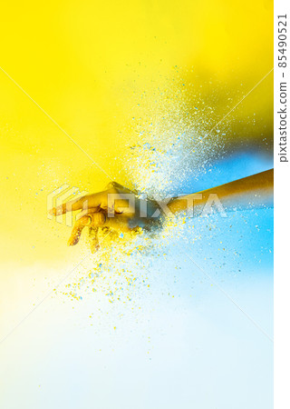 Yellow and white. Female hand and explosion of colored, neoned powder on bright studio background with copy space. Magazine cover, wallpaper design Yellow and white. Female hand and explosion of colored, neoned powder on bright studio background with copy space. Magazine cover, wallpaper design 85490521