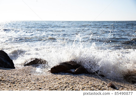 Waves crashing against the rocks from the blue sea beyond the horizon Waves crashing against the rocks from the blue sea beyond the horizon 85490877